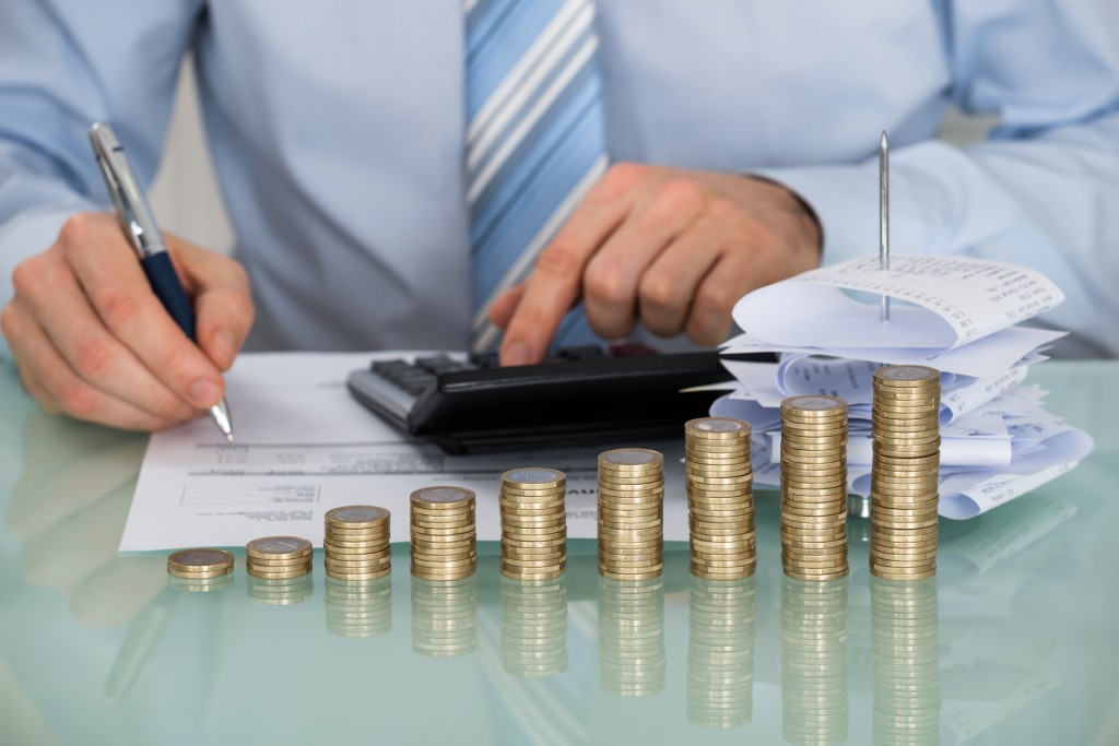 Businessman Calculating Bills In Front Of Stacked Coins