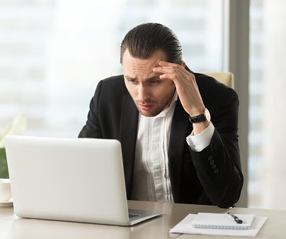 Upset confused businessman looking at laptop screen at workplace.