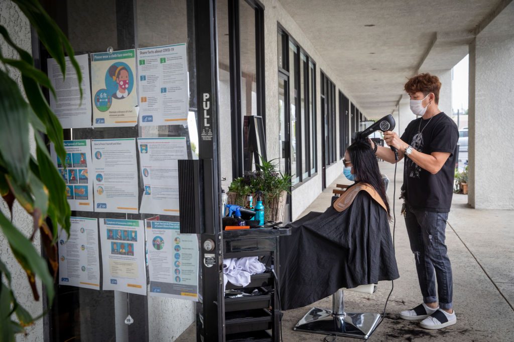 Travis Vu cuts a clients hair outdoors in front of his TravisVu The Salon, as mandated by Gov. Newsom on Monday.